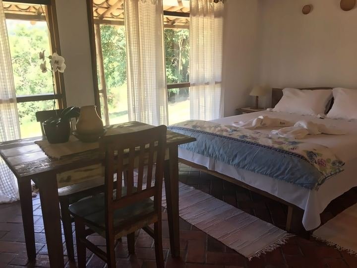 Quarto com cortinas claras e janelas para a mata