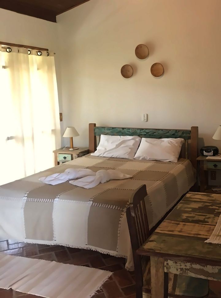 Interior do chalé com cama, luminárias e porta do banheiro